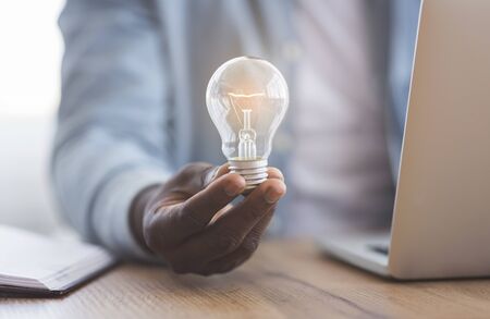 New idea concept. Unrecognizable black businessman holding illuminated light bulb in hand while...