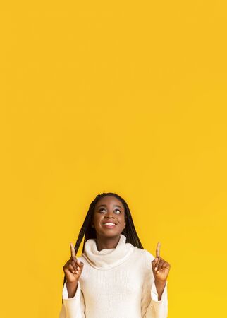 Cheerful african american woman pointing up at free space, yellow backgroundの写真素材