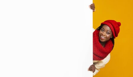 Empty Space For Advertising. Black cheerful girl in red knitted set staying next to empty yellow board, yellow backgroundの写真素材