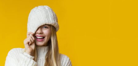Offer, deal, sale concept. Pretty girl in winter hat flirting over yellow studio background,...