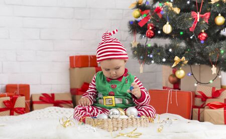 Sweet Santa helper playing with holiday decorations under Christmas tree, free space