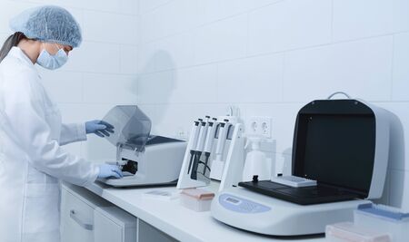 Young woman working in modern laboratory and using analyzer machine, panorama, copy space