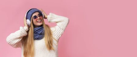 Carefree girl in blue knitted hat and sunglasses listening to music, using wireless headset,...