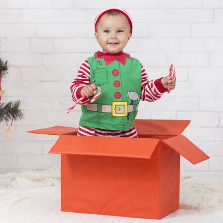 Christmas fun. Adorable Santa helper with lollipops standing in big gift box, free space