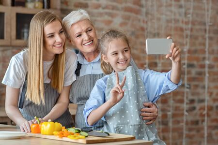 Smiling daughter, mom and granny taking selfie while making healthy food together, empty space