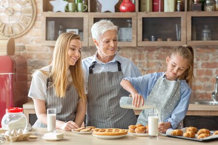 Care, bonding, affectionate concept. Cute little girl pouring milk to granny and mom at kitchen,...
