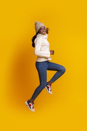Active afro winter girl jogging in the air over yellow studio backgroundの写真素材