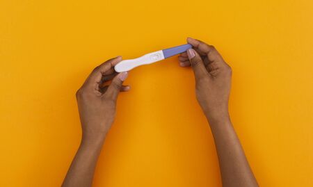 Baby planning concept. Pregnancy or ovulation test with blank result place in african american womans hands over orange background, panoramaの写真素材