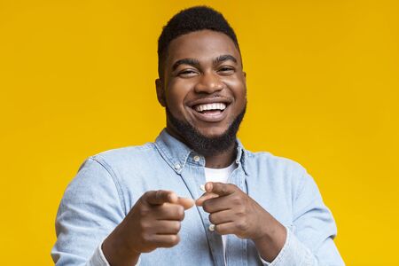 You are next. Cheerful african american man pointing fingers at camera on yellow studio background, copy spaceの写真素材
