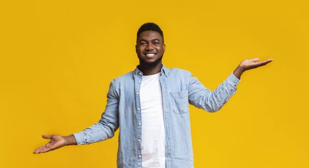 Make right choice. Handsome black man comparing variants, making scales with his empty hands over yellow studio background, panoramaの写真素材