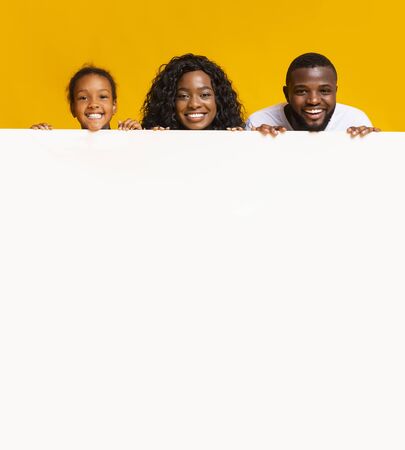 Offer for families. African american parents and little daughter leaning on blank white advertisement board with free spaceの写真素材