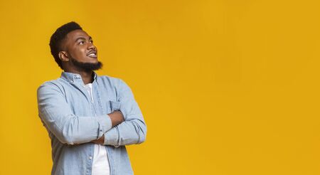 Interesting offer. Handsome black guy looking upwards at copy space on yellow studio background, panoramaの写真素材