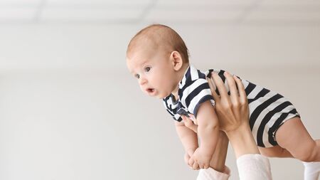 Portrait of funny newborn baby lifted in air by mother, panorama with free spaceの写真素材