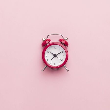 Minimalism concept. Red toy alarm clock on pink background, copy spaceの写真素材
