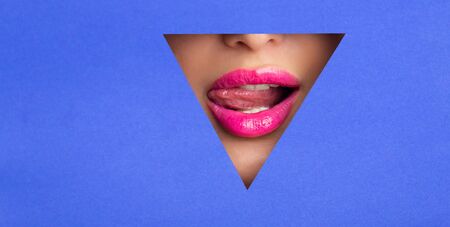 Sexy woman with pink lips playing with tongue in blue paper hole, empty spaceの写真素材