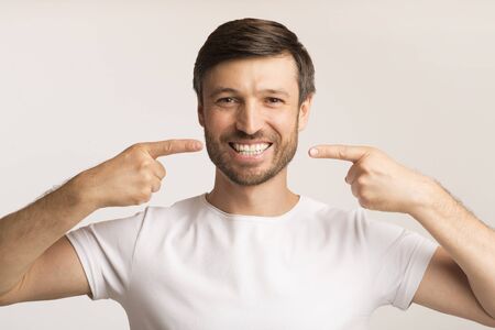 Dental Care Concept. Middle-Aged Man Pointing Fingers At His Smile Showing Perfect Teeth Standing Over White Studio Backgroundの写真素材
