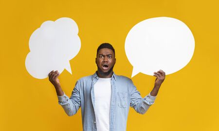 Complex choice. Confused black guy holding two speech bubbles on yellow background, panorama