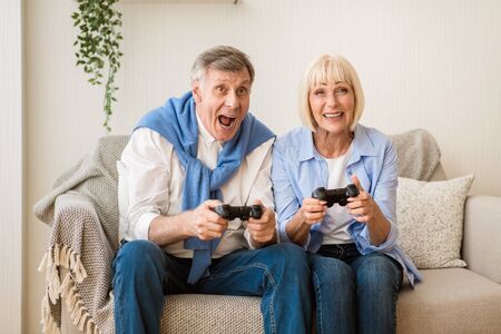 Overjoyed mature couple playing video games at home, having fun on weekends