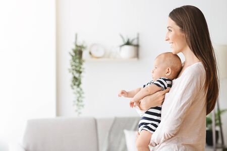 Beeing a mom. Beautiful young woman holding adorable newborn baby in arms, side view