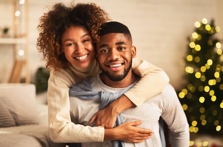 Christmas eve. Loving couple embracing and smiling to camera in front of Christmas treeの写真素材