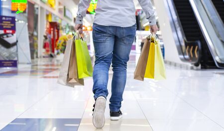 Shopping concept. Guy walking in shopping mall with paper bags, crop, back viewの写真素材