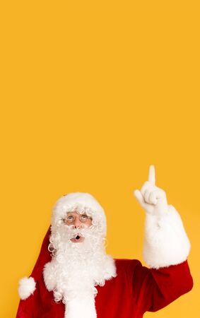 Surprised Santa Claus indicating at copy space on orange background, vertical panoramaの写真素材