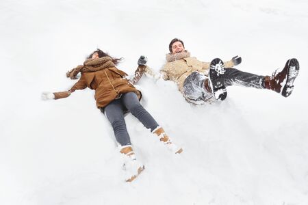 Winter. Young Couple Lying In Snow And Laughing Having Fun Outdoor. Selective Focus