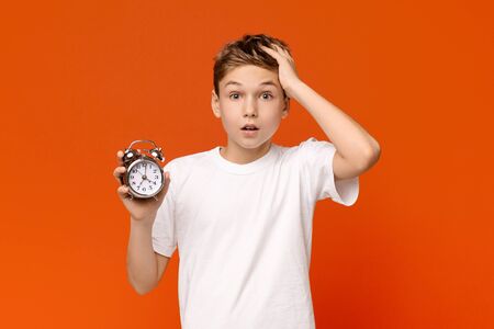 Overslept. Worried awake teen boy with alarm clock is shocked because it is too lateの写真素材