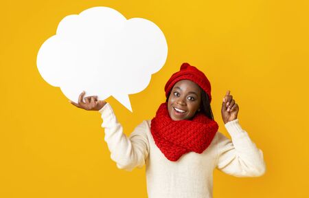 Cheerful afro girl in winter hat with communication bubble pointing finger up, got good idea, yellow...