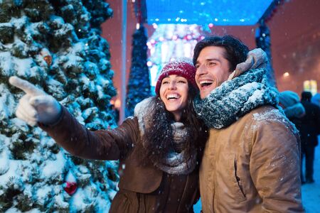 Happy Girl Pointing Finger Showing Something Boyfriend Standing On Outdoor Xmas Market In Eveningの写真素材
