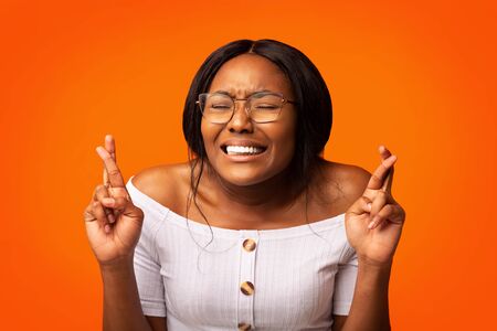 Black Girl Keeping Fingers Crossed For Luck Being Afraid Or Making A Wish Standing Over Orange...