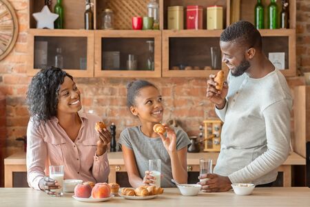 Friendly young african american family having conversation during breakfast at kitchen, happy cozy atmosphere, copy spaceの写真素材