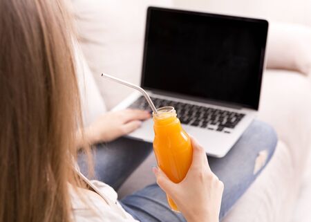 Woman working on laptop with black blank screen and drinking detox cocktail, copy spaceの写真素材