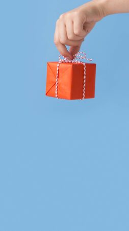 Celebrating Christmas. woman holding red box with gift over blue background, vertical panorama, copy spaceの写真素材