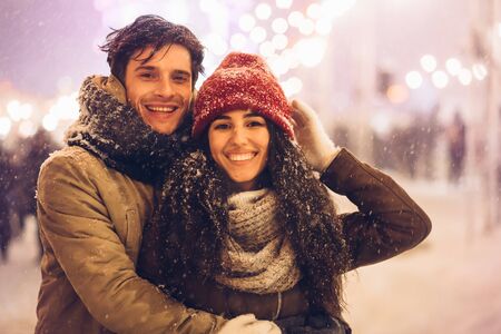 Xmas Mood. Loving Couple Embracing Smiling At Camera Standing Outdoor On Christmas Market At Nightの写真素材