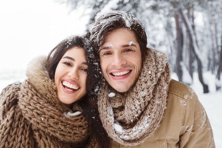 Merry Christmas. Couple With Snow In Hair Hugging And Smiling At Camera Standing In Winter Forest