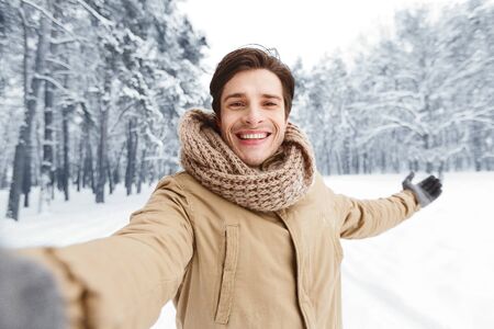 Happy Man Taking Selfie Standing In Snowy Forest in Morning. Selective Focusの写真素材