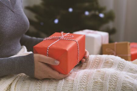 Girl holding her Christmas present in hands and sitting on the bed, blurred background, copy spaceの写真素材