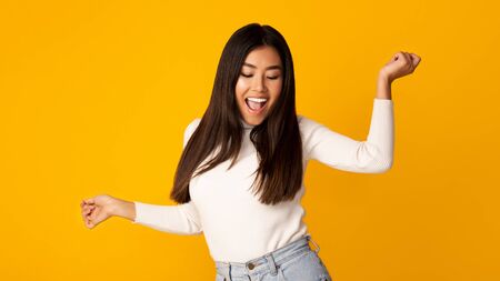 Happy asian woman dancing on yellow studio background, panoramaの写真素材