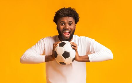 Excited african american football fan with ball on orange background, copy spaceの写真素材