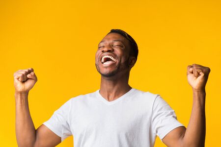 Happy Black Man Screaming In Delight And Shaking Fists Standing Over Yellow Studio Background.の写真素材