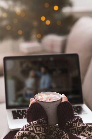 Female with cup of hot chocolate watching on laptop screen, vertical panorama, blurred background, copy spaceの写真素材