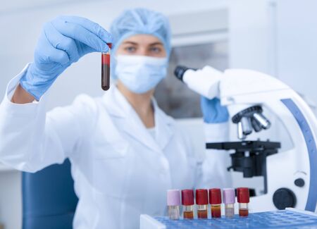 Young female scientist holding tube with blood sample, blurred motion, laboratory interior