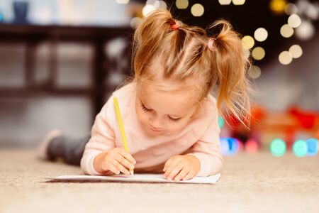 Little girl drawing letter to Santa Claus, lying on floor near Christmas tree, empty spaceの写真素材