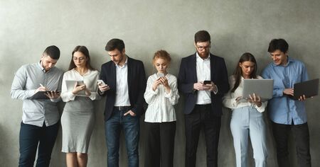 Business people with gadgets standing in row over grey wall, panoramaの写真素材
