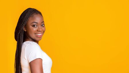 Smiling african girl looking at camera over shoulder, yellow background, panorama with free spaceの写真素材