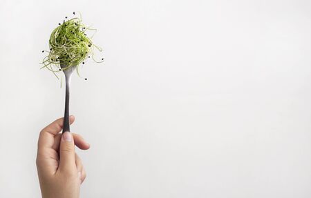 Symbol of health. Woman holding microgreens on fork isolated on white background, copy space