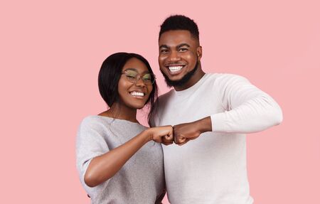 Happy smiling black couple bumping fists, cooperation and teamwork concept, pink studio backgroundの写真素材