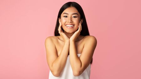 Young asian girl touching her smooth cheeks, caring about her skin on pink studio background, panoramaの写真素材