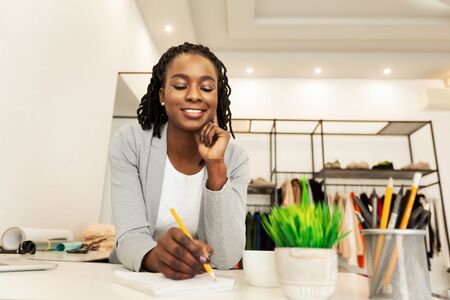 Happy Black Dressmaker Drawing Sketches Working In Clothing Atelier. Selective Focus, Free Spaceの写真素材